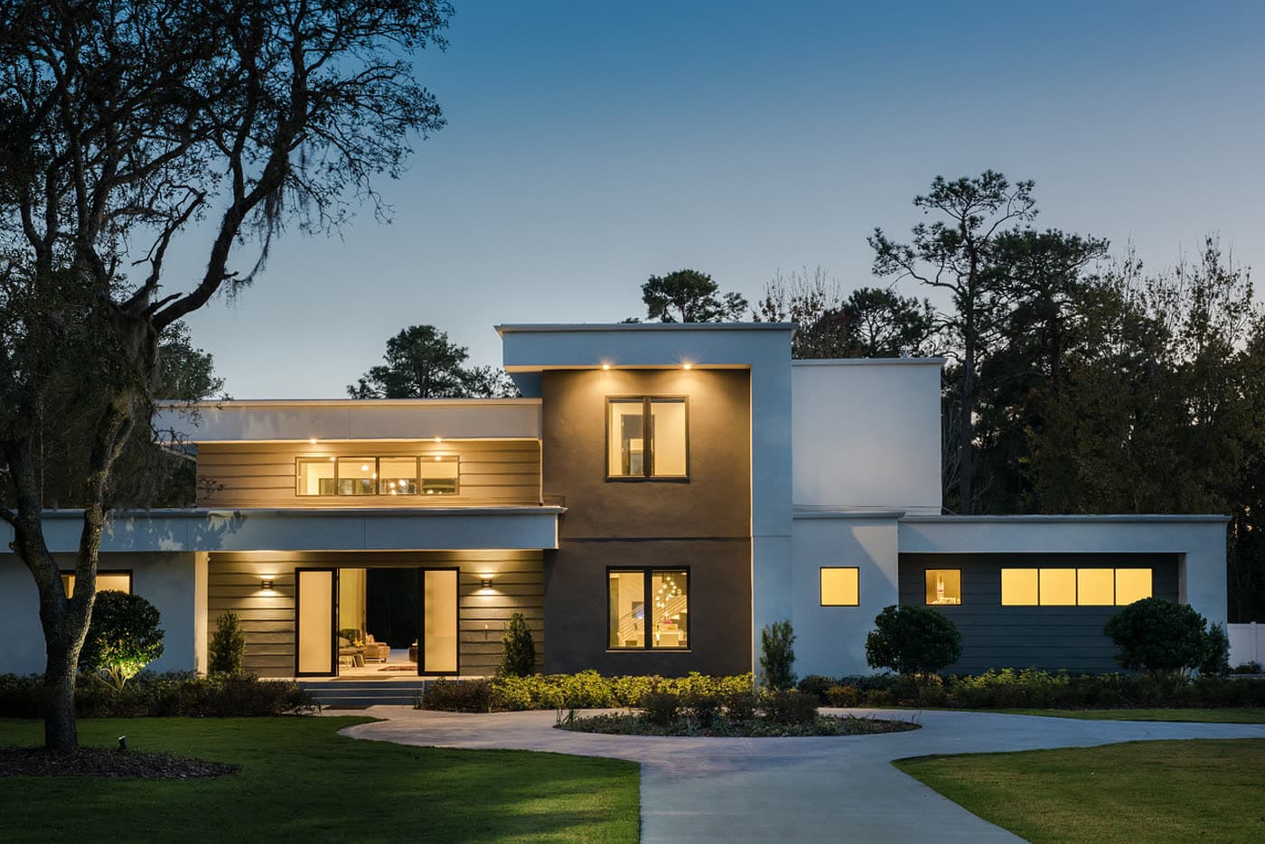 A lit driveway and front entrance of a contemporary home at dusk